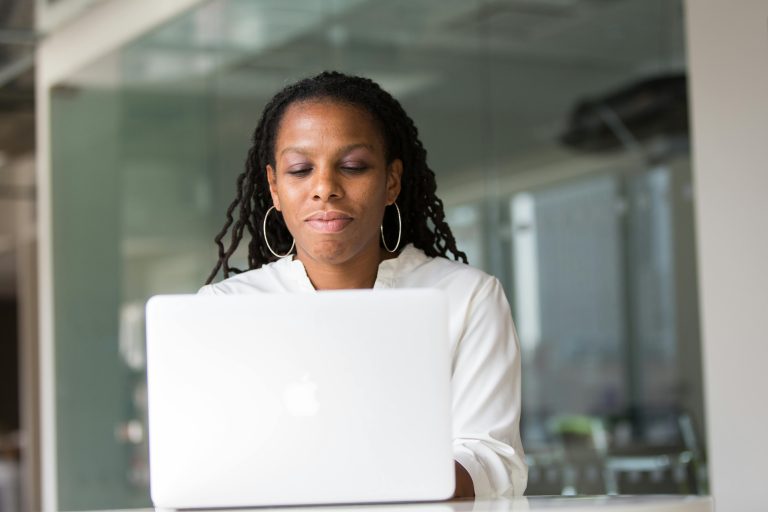Focused African American woman working remotely on a laptop in a contemporary office setting.